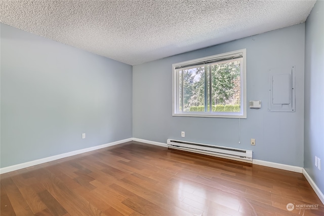 spare room featuring a textured ceiling, electric panel, hardwood / wood-style floors, and a baseboard heating unit