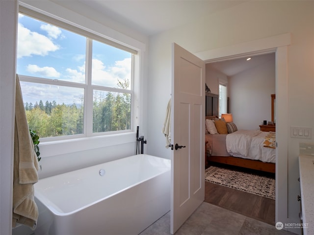 bathroom with wood-type flooring, lofted ceiling, a washtub, and a healthy amount of sunlight