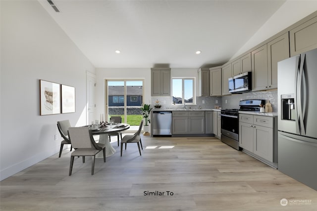 kitchen featuring stainless steel appliances, light hardwood / wood-style floors, decorative backsplash, gray cabinets, and vaulted ceiling