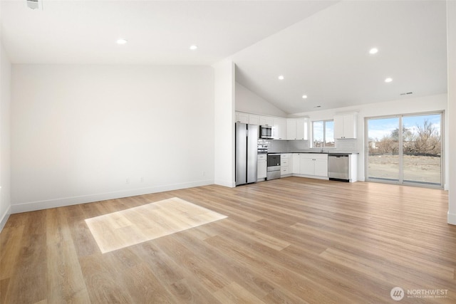 unfurnished living room featuring baseboards, lofted ceiling, light wood-style flooring, a sink, and recessed lighting