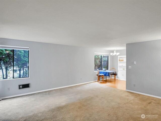 unfurnished room featuring carpet and an inviting chandelier