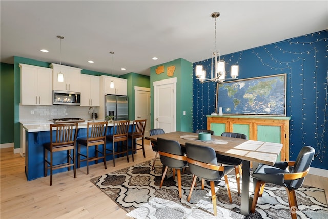 dining area with light wood-type flooring, a chandelier, and sink