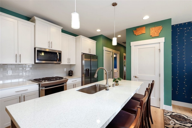 kitchen with an island with sink, sink, decorative light fixtures, white cabinetry, and stainless steel appliances