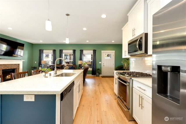 kitchen featuring appliances with stainless steel finishes, white cabinetry, decorative light fixtures, a kitchen island with sink, and sink