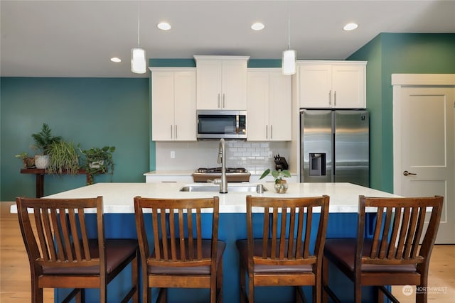 kitchen with decorative backsplash, light hardwood / wood-style floors, an island with sink, white cabinets, and stainless steel appliances