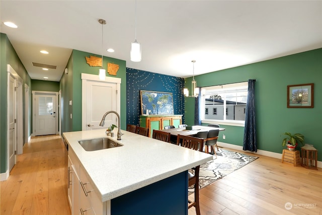 kitchen featuring hanging light fixtures, an inviting chandelier, light hardwood / wood-style flooring, a kitchen island with sink, and sink