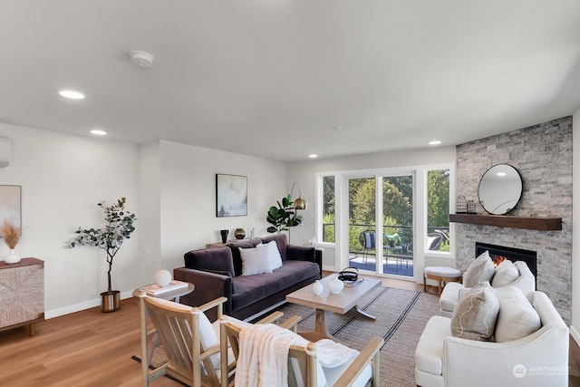 living room featuring a fireplace, light hardwood / wood-style flooring, and a wall unit AC