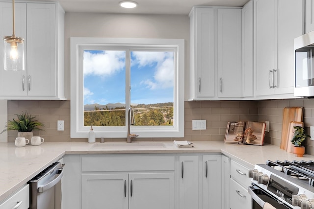 kitchen featuring tasteful backsplash, sink, white cabinets, stainless steel appliances, and decorative light fixtures