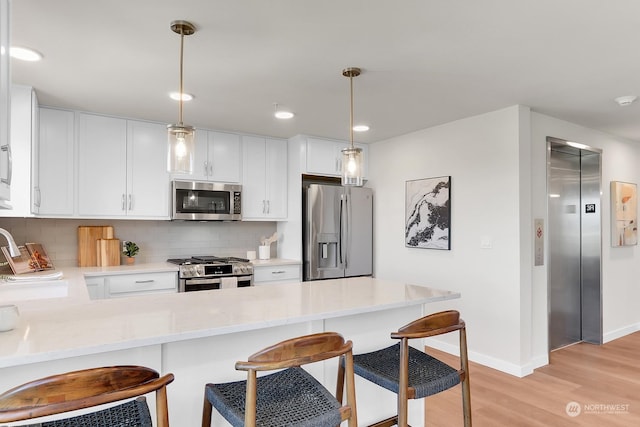 kitchen with white cabinetry, kitchen peninsula, pendant lighting, stainless steel appliances, and light hardwood / wood-style flooring