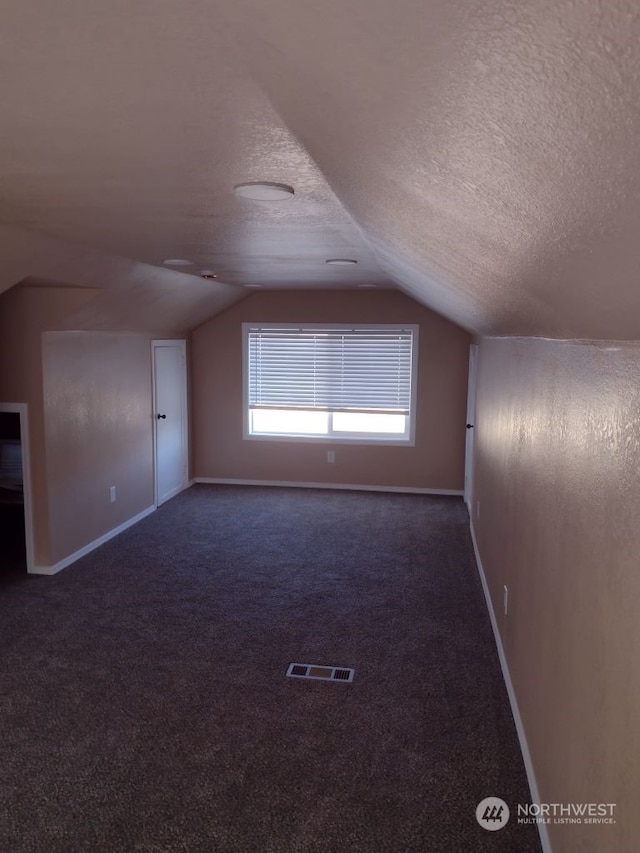 bonus room featuring dark carpet, a textured ceiling, and lofted ceiling