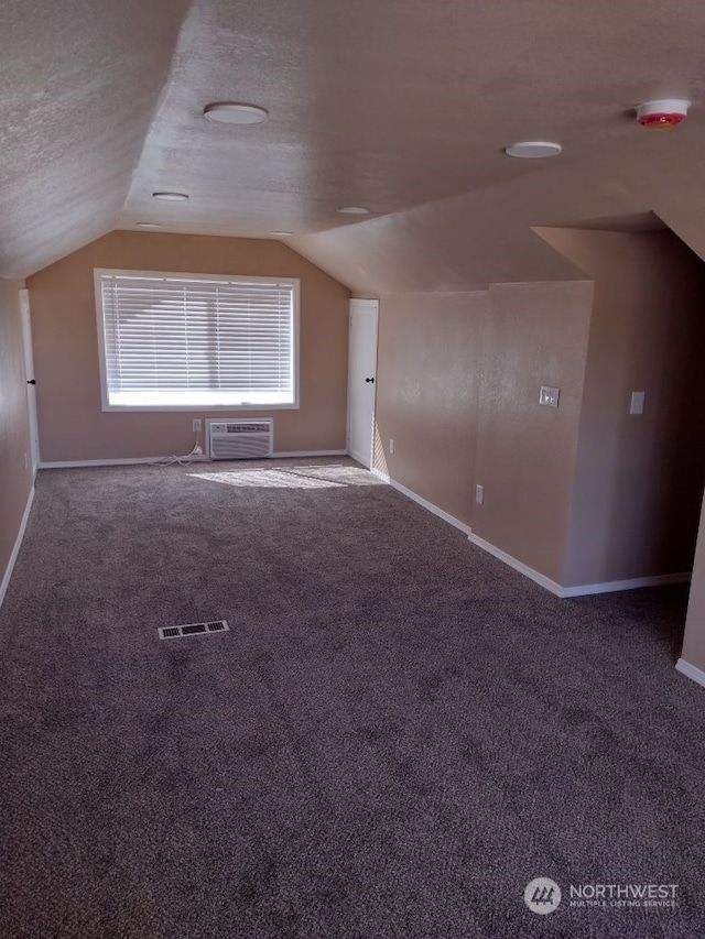 additional living space with a textured ceiling, carpet, lofted ceiling, and an AC wall unit