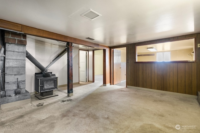 basement with a wood stove, wood walls, and light colored carpet