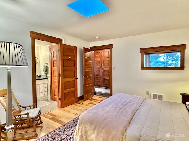 bedroom with light wood-style floors, ensuite bath, and visible vents