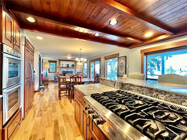 kitchen with light stone counters, pendant lighting, beamed ceiling, light hardwood / wood-style flooring, and stainless steel appliances