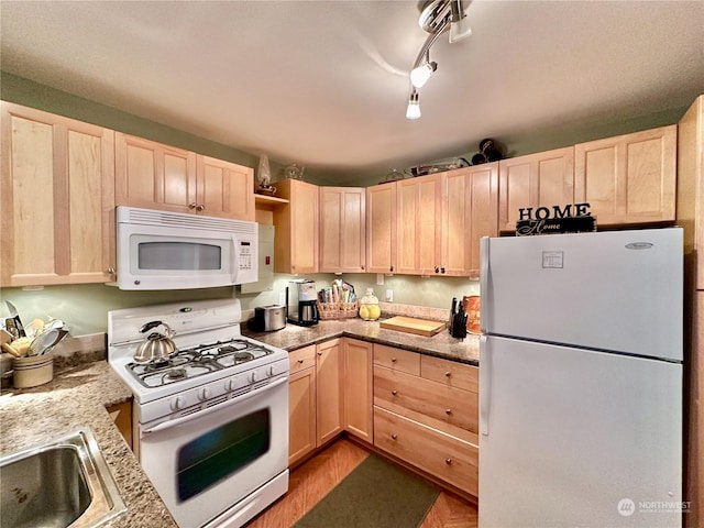 kitchen featuring light stone counters, a sink, light brown cabinetry, and white appliances