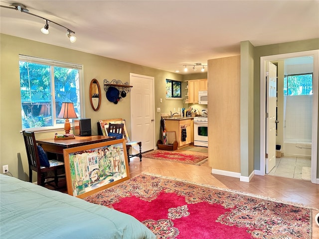 bedroom featuring track lighting, ensuite bath, and light parquet flooring