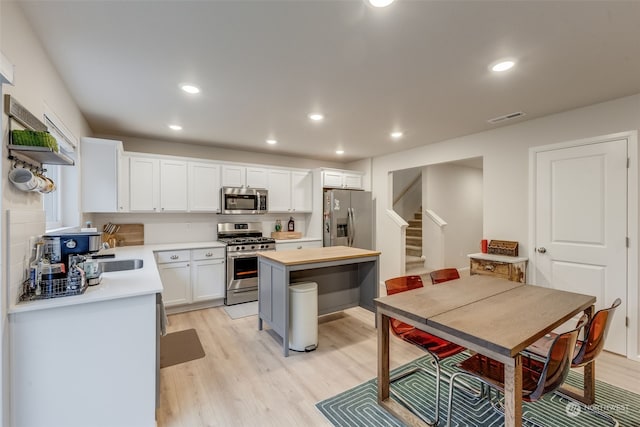 kitchen with white cabinets, sink, stainless steel appliances, a center island, and light hardwood / wood-style floors