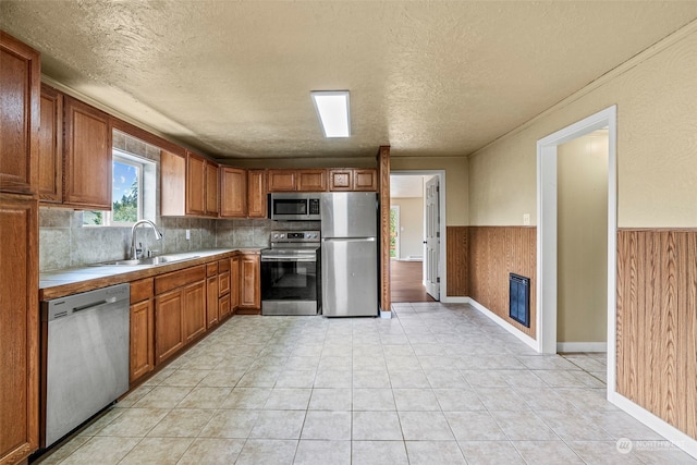 kitchen featuring sink, tasteful backsplash, a textured ceiling, wooden walls, and stainless steel appliances