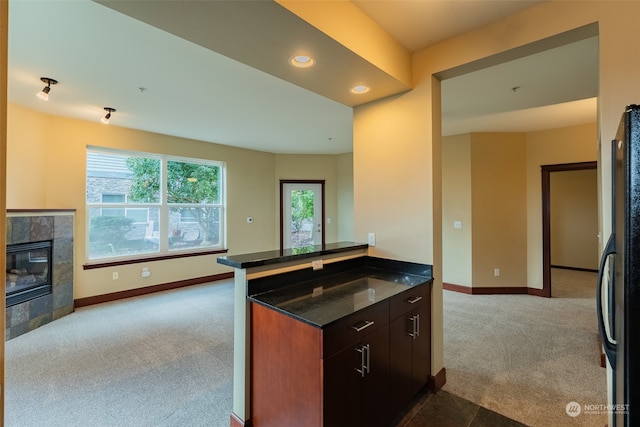 kitchen with dark brown cabinetry, light carpet, black fridge, a fireplace, and kitchen peninsula