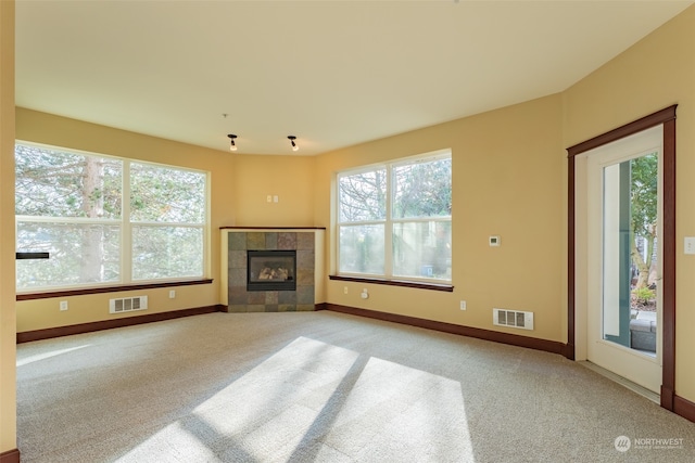 unfurnished living room featuring plenty of natural light, a tile fireplace, and light carpet