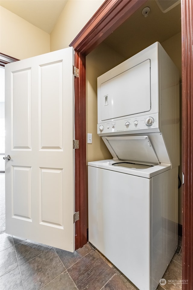 laundry room with dark tile patterned floors and stacked washing maching and dryer