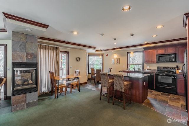 kitchen with crown molding, decorative light fixtures, a fireplace, black appliances, and a center island