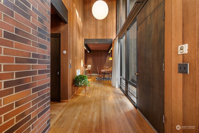 hall featuring brick wall, light wood-type flooring, wood walls, and a high ceiling