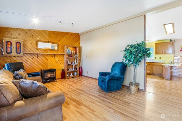 living room featuring light hardwood / wood-style flooring, wooden walls, a wood stove, and track lighting