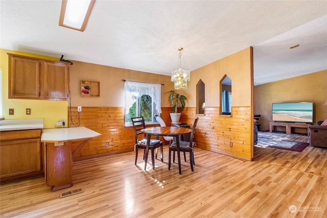 dining space featuring a notable chandelier, light hardwood / wood-style flooring, and wood walls