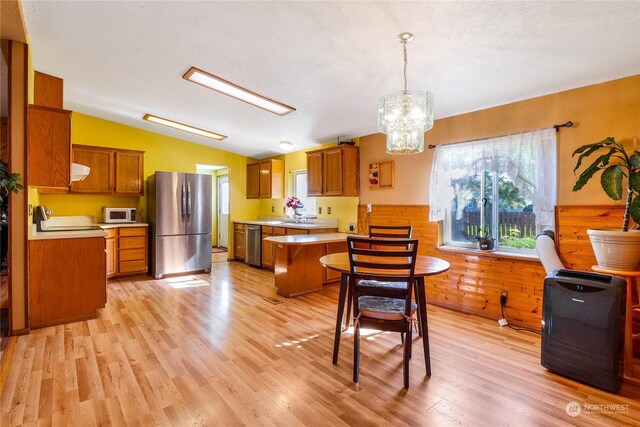 kitchen with light hardwood / wood-style floors, decorative light fixtures, appliances with stainless steel finishes, an inviting chandelier, and vaulted ceiling