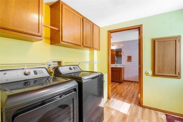 washroom featuring cabinets, light wood-type flooring, washing machine and clothes dryer, and sink