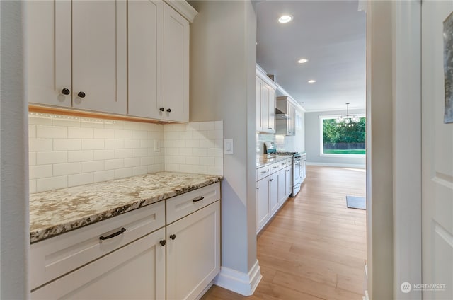 kitchen featuring decorative backsplash, light hardwood / wood-style floors, white cabinetry, light stone countertops, and stainless steel range with gas cooktop