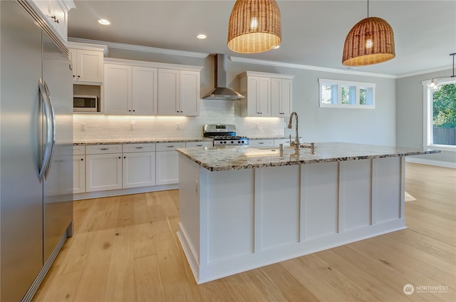 kitchen featuring white cabinets, an island with sink, hanging light fixtures, wall chimney range hood, and appliances with stainless steel finishes