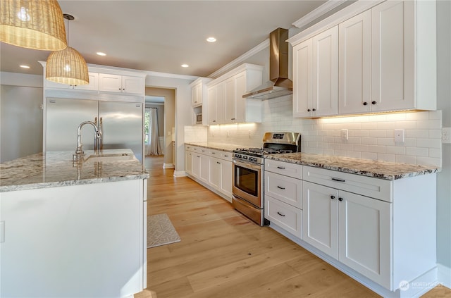 kitchen featuring appliances with stainless steel finishes, white cabinetry, wall chimney range hood, and decorative light fixtures