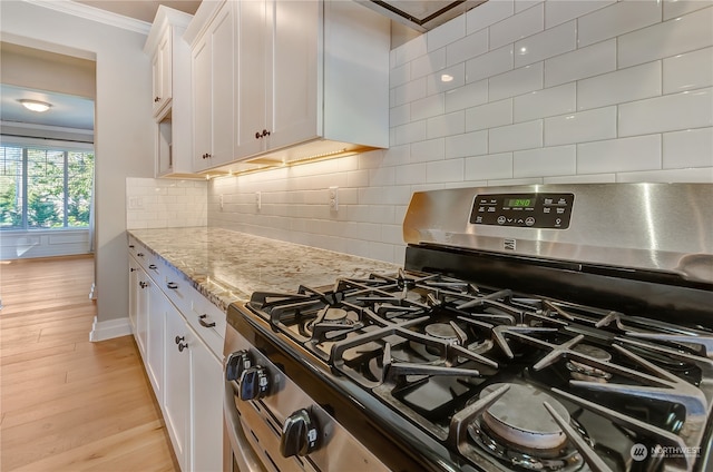 kitchen featuring light stone counters, light hardwood / wood-style floors, white cabinetry, gas range, and crown molding