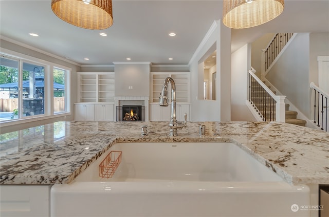 kitchen with ornamental molding, sink, light stone counters, and decorative light fixtures