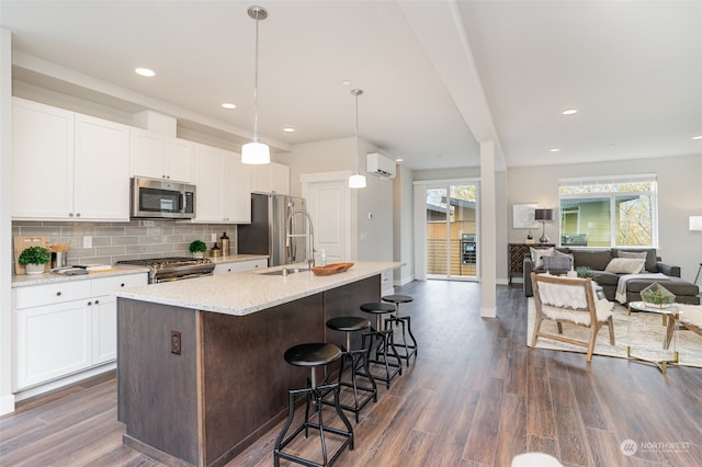 kitchen featuring hanging light fixtures, an island with sink, appliances with stainless steel finishes, white cabinetry, and dark hardwood / wood-style floors