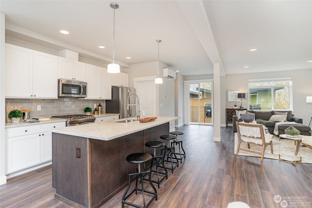 kitchen featuring white cabinets, hanging light fixtures, a center island with sink, dark hardwood / wood-style flooring, and appliances with stainless steel finishes