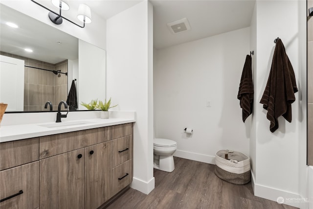 bathroom with tiled shower, hardwood / wood-style floors, vanity, and toilet