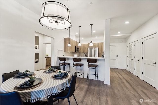 dining area featuring dark wood-type flooring, sink, and an inviting chandelier