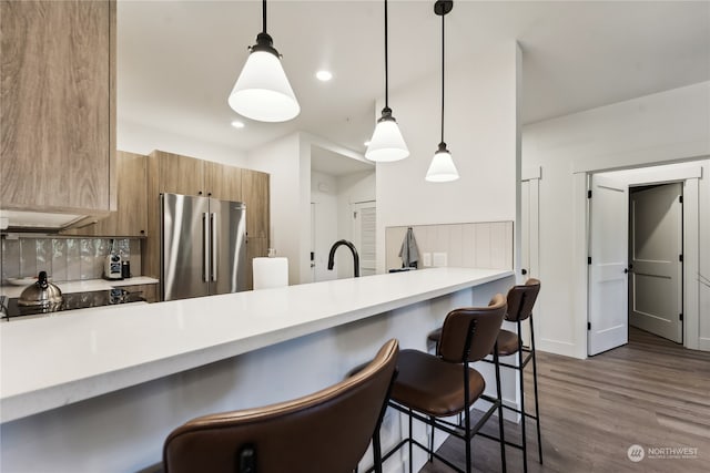 kitchen with stainless steel refrigerator, dark wood-type flooring, kitchen peninsula, hanging light fixtures, and a kitchen bar