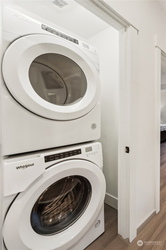 laundry room featuring stacked washer / drying machine and dark hardwood / wood-style flooring