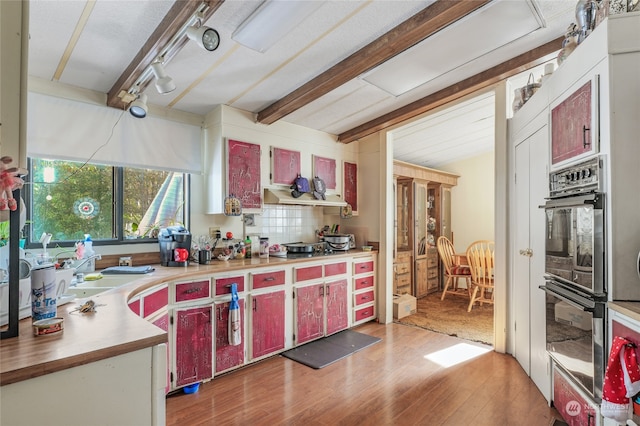 kitchen with backsplash, track lighting, black double oven, dark wood-type flooring, and beamed ceiling