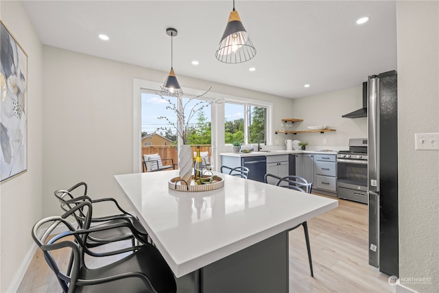 kitchen featuring decorative light fixtures, a breakfast bar area, appliances with stainless steel finishes, and light hardwood / wood-style flooring