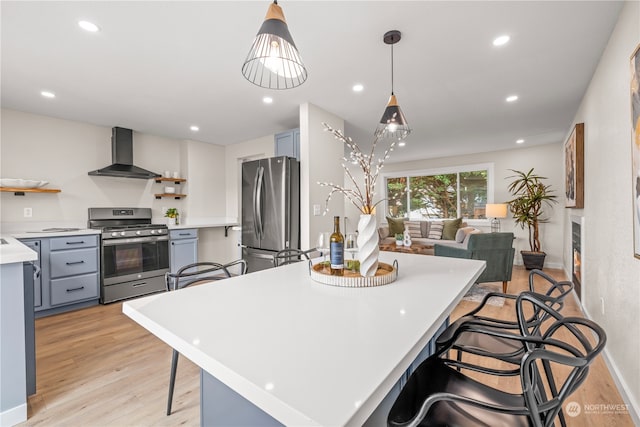 kitchen featuring pendant lighting, light hardwood / wood-style floors, a kitchen bar, wall chimney range hood, and stainless steel appliances