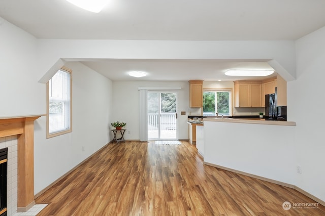 kitchen featuring a fireplace, light brown cabinets, wood-type flooring, sink, and black fridge