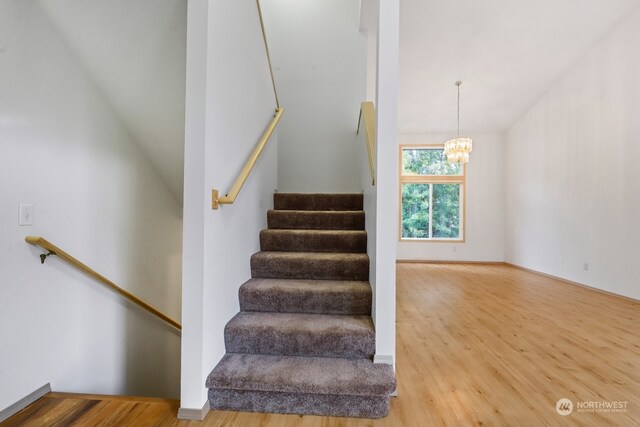 stairway with wood-type flooring and a notable chandelier