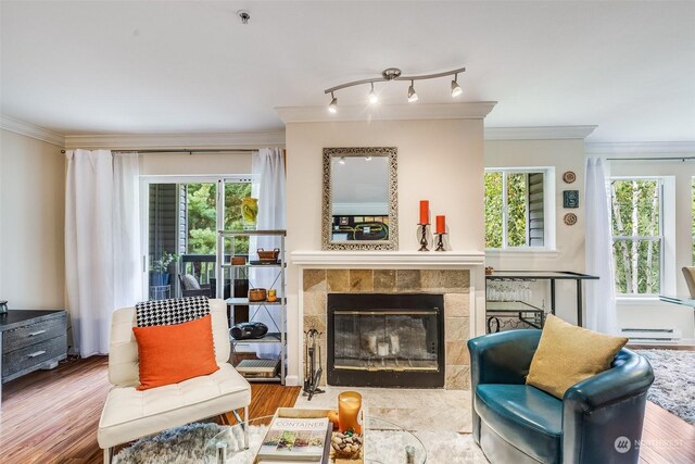 living room featuring ornamental molding, baseboard heating, hardwood / wood-style floors, and a tile fireplace