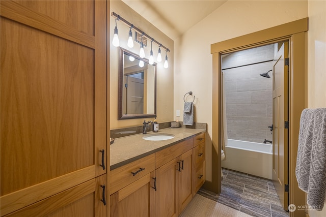 bathroom with hardwood / wood-style flooring, vanity, vaulted ceiling, and tiled shower / bath