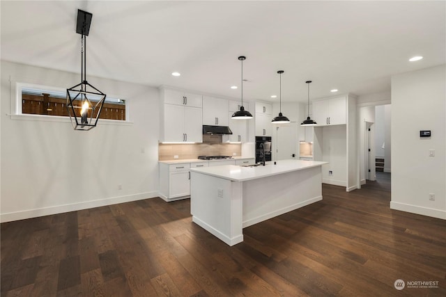 kitchen featuring under cabinet range hood, backsplash, light countertops, baseboards, and white cabinetry